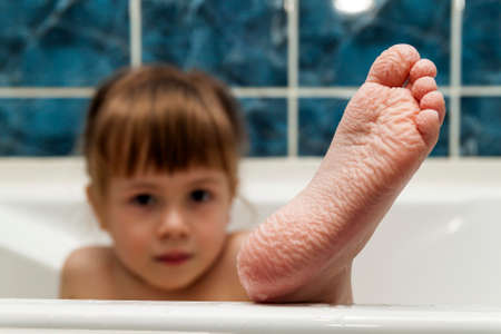 Wrinkled bare feet coming out from a bathtub. Young person getting a bath feet close-up indoor in bathroom interrior photoの写真素材