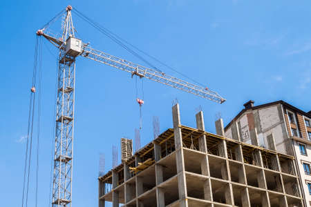 Modern building under construction against blue sky. Tower crane construction work siteの写真素材