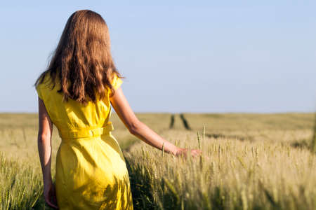 Beauty young girl outdoors enjoying nature. Beautiful teenage model girl in yellow dress walking on the wheat field in sun light.の写真素材
