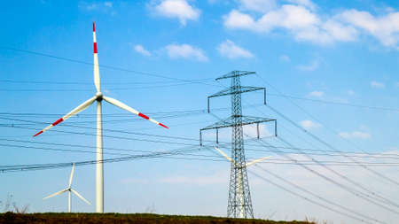 High voltage tower and wind turbines against blue skyの写真素材