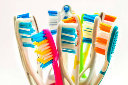 Close up shot of set of multicolored toothbrushes in glass on clean toilet on white background,...