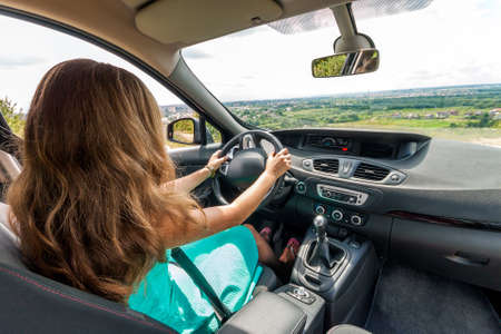 Girl in dress with red hair driving a car. Rear viewの写真素材