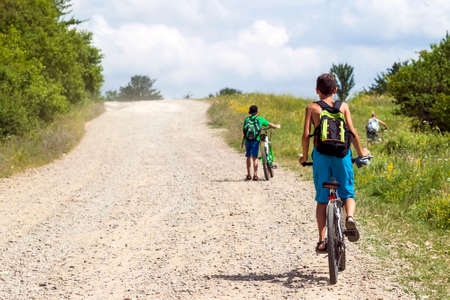 Children boys riding bicycles on a gravel road on a sunny dayの写真素材
