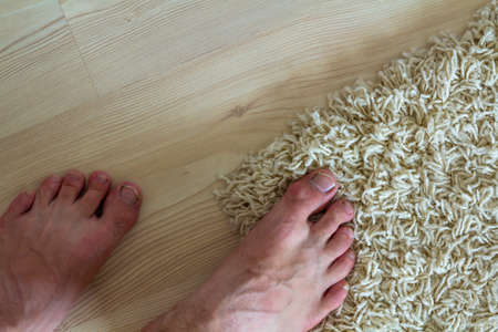 Human bare feet standing on the floor. One foot on carpet and another on laminate parquet