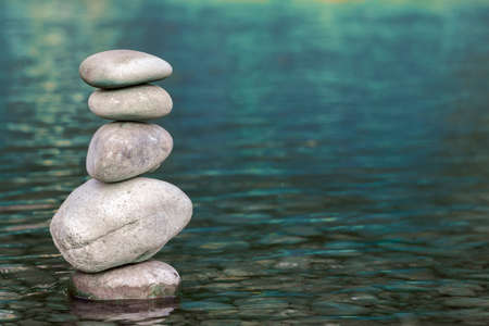 Stack of stones balancing on top in blue water of the riverの写真素材