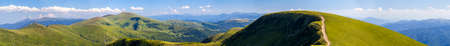 Panorama of green hills in summer mountains with gravel road for travelling by carの写真素材