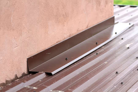 Roofing construction detail close-up. Metal panel on house roof near wall