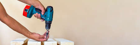 Hand of a worker screws a screw in a wooden board with a cordless screwdriver. Man carpenter at handmade workの写真素材