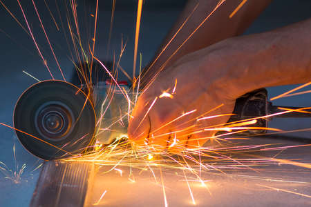 Close-up of worker hands cutting metal with grinder. Sparks while grinding iron. Low depth of focusの写真素材