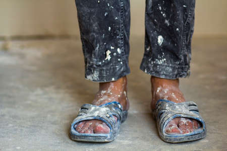 Feet of a construction worker in old dirty clothes and shoesの写真素材