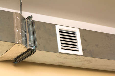 Ventilation pipes in silver insulation material hanging from the ceiling inside new building.