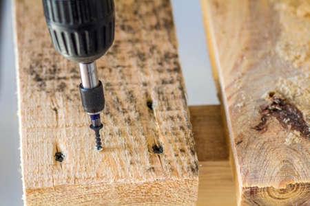 Workers hand with electric screwdriver screwing a screw into wooden boardの写真素材