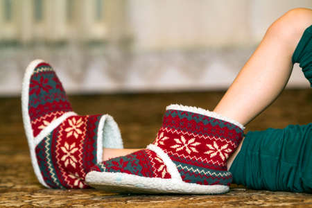 Bare child legs and feet in red winter christmas boots with ornament patternの写真素材