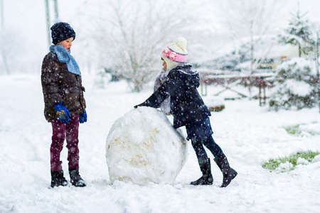 Children boy and girl outdoors in snowy winter are making a big snowman