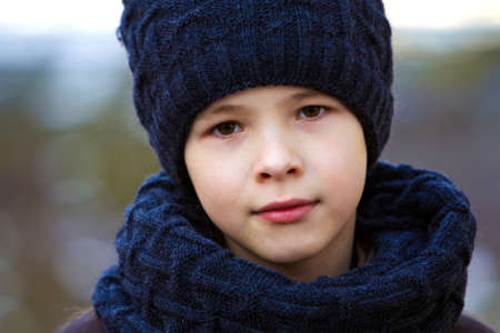 Portrait of child boy in hat and scarf outdoors in sunny winter dayの写真素材