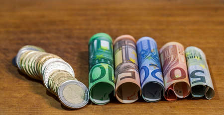 Five, ten, twenty, fifty and one hundred euro rolled bills banknotes, with euro coins on wooden table background.の写真素材