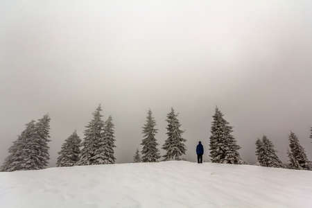 Man hiker standing in winter snow covered mountains enjoying view