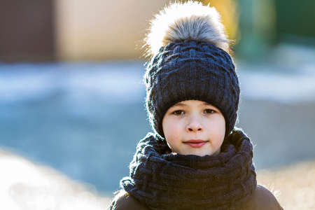 Portrait of child boy in hat and scarf outdoors in sunny winter dayの写真素材