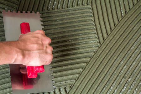 Worker hand with trowel tool for tiles installation making mortar adhesive on floor