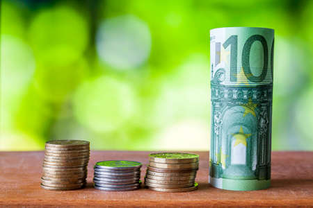 One hundred euro rolled bill banknote with euro coins on wooden table background.の写真素材