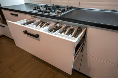 Stainless steel spoons, forks and knifes in cutlery box drawer in white kitchen cupboard.の写真素材
