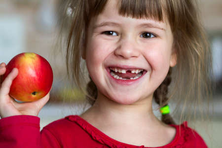 A cute little curly toothless girl smiles and holds a red apple.の写真素材