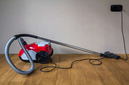 Red modern vacuum cleaner with black electric cable on wooden parquet floorの写真素材