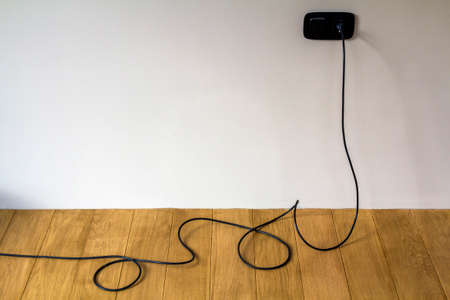 Black electric cable in wall socket on wooden parquet floorの写真素材
