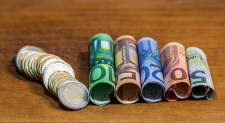 Five, ten, twenty, fifty and one hundred euro rolled bills banknotes, with euro coins on wooden table background.の写真素材