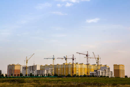 Construction site of a new apartment high building with tower cranes against blue sky. Residential area development. Real estate project growth concept.の写真素材