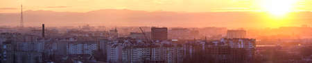 Panoramic view of beautiful yellow golden sunset over Ivano-Frankivsk city, Ukraine. Evening urban landscape with high buildings and towers covered in setting sun beams. Far away mountains before nightの写真素材