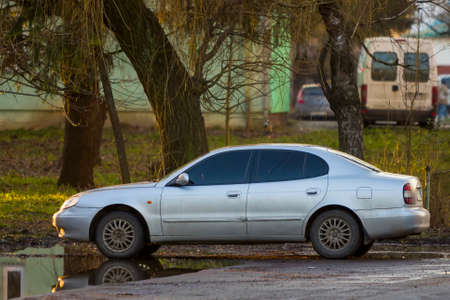 A new white car standing under shadowy green tree on summer bright day.の写真素材