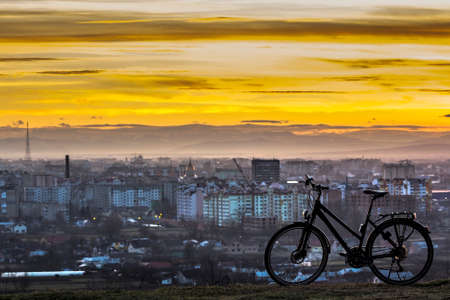 Modern sports city bicycle standing alone over night city background with many bright lights. View of orange sunset sky in Ivano Frankivsk city, Ukraineの写真素材