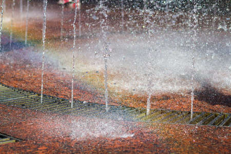 Close up of beautiful city fountain. Splashing upward crystal thin streams of clear cool transparent water, shiny droplets. Multicolored blurred rainbow, recreation area.の写真素材