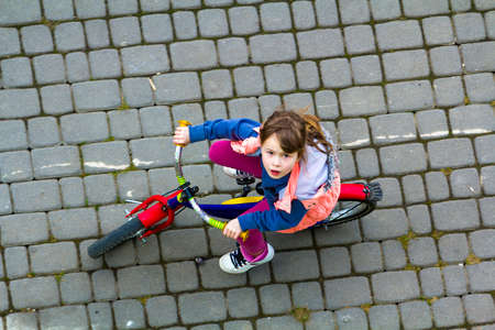 Top view of pretty young girl with long light brown hair riding a bicycle on cool spring day looking...
