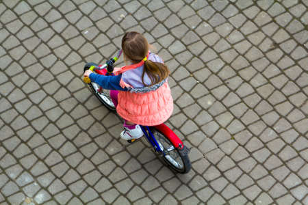 Top view of pretty young girl with long light brown hair riding a bicycle on cool spring day looking upward. Outdoors activities.healthy lifestyle and happy childhood.の写真素材