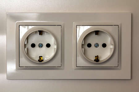 New white shiny plastic electric double sockets on white wall background. Advantages and comfort of...