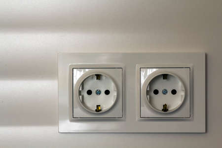 New white shiny plastic electric double sockets on white wall background. Advantages and comfort of modern homes.の写真素材