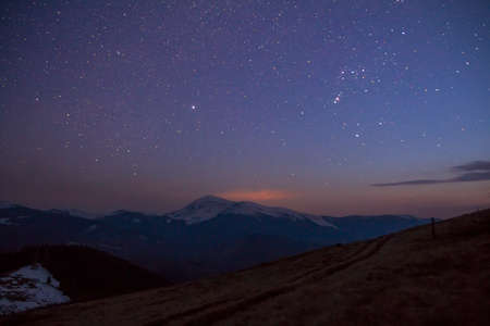 Majestic view of fantastic starry dark sky over magnificent Carpathian mountains covered with evergreen forest and snow-capped peaks in distance. Breathtaking panorama of beauty and magic of nature.の写真素材