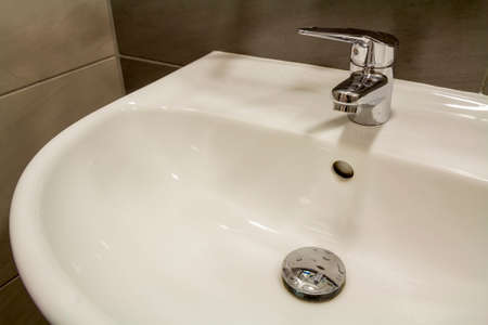 Close-up of new modern ceramic clean empty white washbasin sink connected to the sewer on background of nice light beige ceramic tiles. Professional plumbing and installation concept.の写真素材
