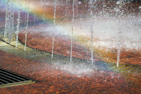 Close up of beautiful city fountain. Splashing upward crystal thin streams of clear cool transparent water, shiny droplets. Multicolored blurred rainbow, recreation area.の写真素材