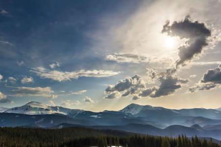 Beautiful fantastic view of blue sky with bright white clouds in mysterious shape of question over magnificent mountain rage with snow covered tops and evergreen pine forest. Beauty of nature concept.の写真素材