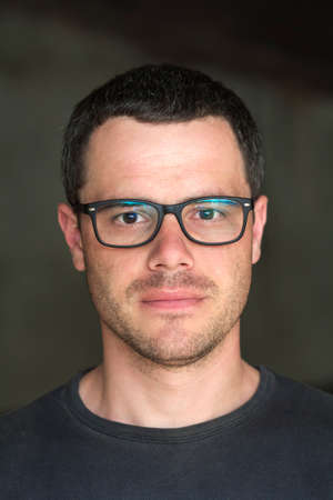 Portrait of young handsome black-haired unshaven confident successful intellectual man in glasses...