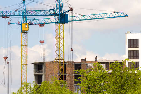 Urban view of silhouettes of two high industrial tower cranes working at construction of new brick...