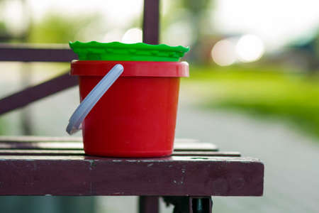 Close-up of plastic baby toy red and green buckets on old brown wooden bench on blurred bright summer bokeh background. Children favorite toys and development activities outdoors concept.の写真素材