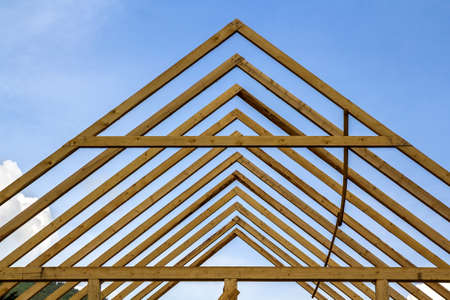 Close-up detail of wooden high steep roof framing under construction. Timber frame of natural materials against bright sky. Professional building and reconstruction concept.の写真素材