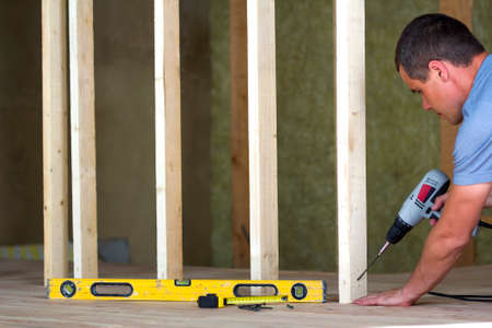 Interior of attic insulated room with oak floor under reconstruction. Young professional worker uses...