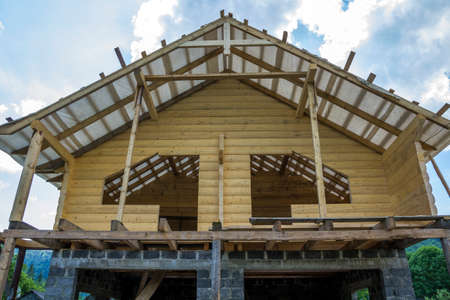 New cottage of natural lumber materials under construction. Wooden walls and roof on high brick...