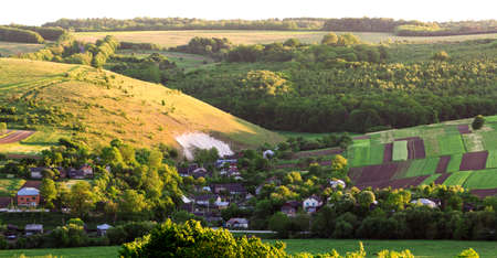 Beautiful wide aerial view of small village among green gardens, patched panorama of dark plowed and...