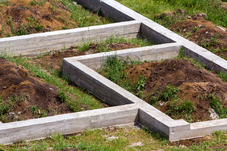 Building site in green field. Close-up detail of trenches dug in ground and filled with cement as...